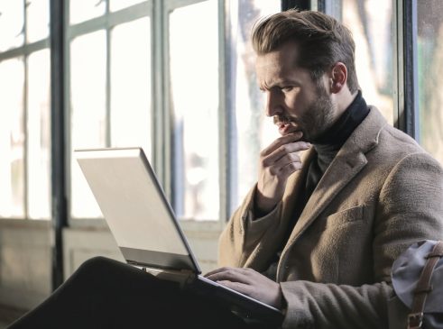 man holding his chin facing laptop computer